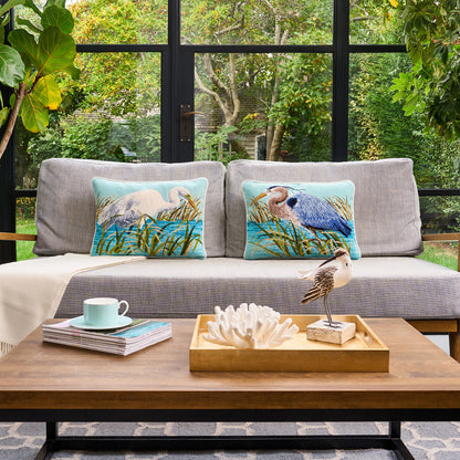 Gray sofa with decorative pillows featuring nature-themed designs, placed in a room with large windows showing greenery outside.