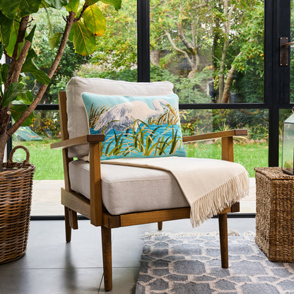 Chair with a decorative pillow and blanket on a patio with greenery outside