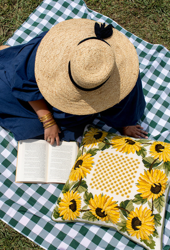 Person reading a book with the provençal sunflower pillow on a picnic blanket