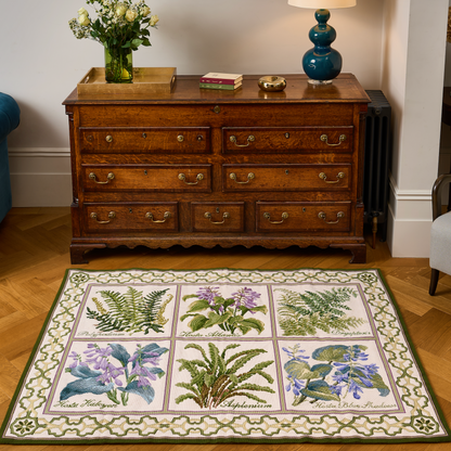 A rectangular area rug with a botanical floral pattern in a 3x3 grid, styled in a living room setting on a wooden parquet floor in front of a dark wood chest of drawers.
