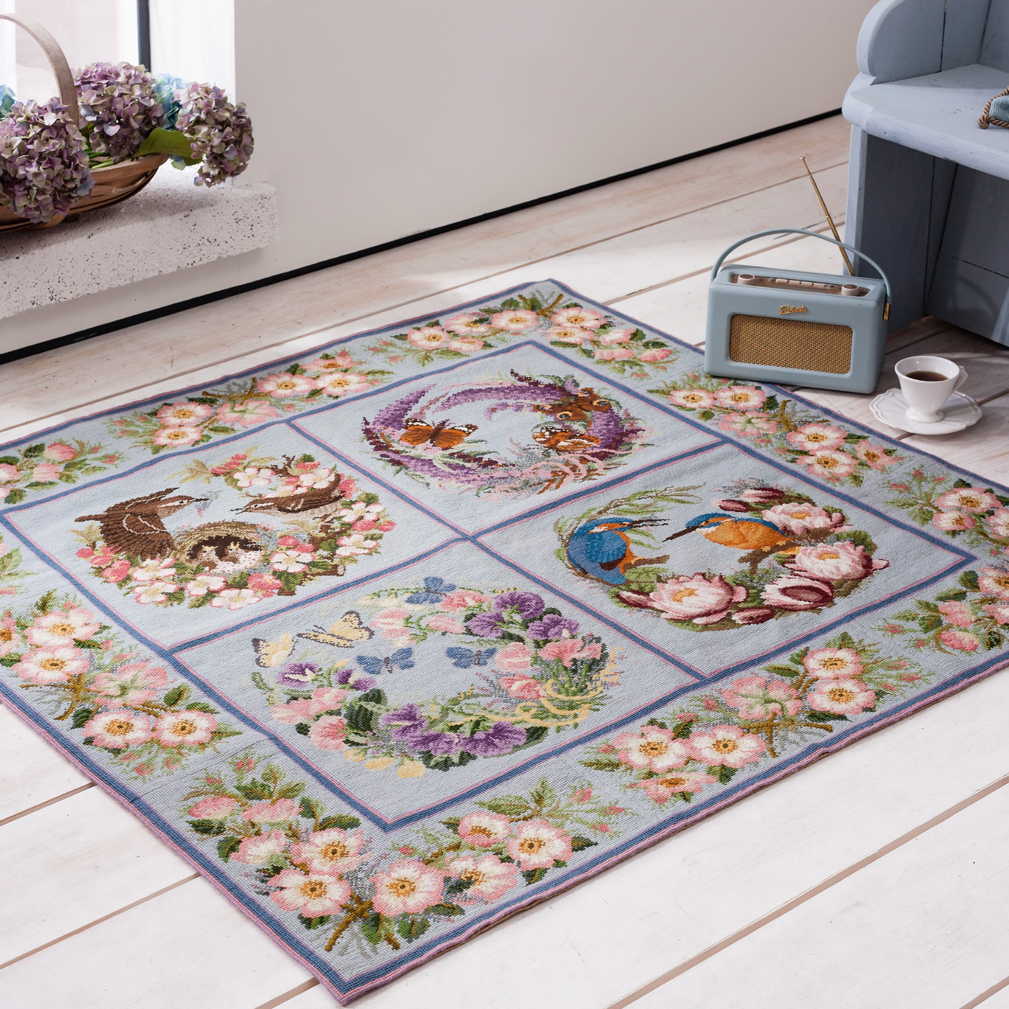Forget me not collection needlepoint carpet with floral motifs, birds and butterflys on a pale blue background